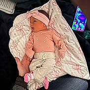 Zariah joined the competition — help win amazing prizes! baby, infant, blanket, pink_clothing, headband, pacifier, smartphone, adult_hand, jeans, patterned_blanket, newborn, lying_down, cute, indoor, soft_lighting, small_feet, person, clothing, accessory, resting