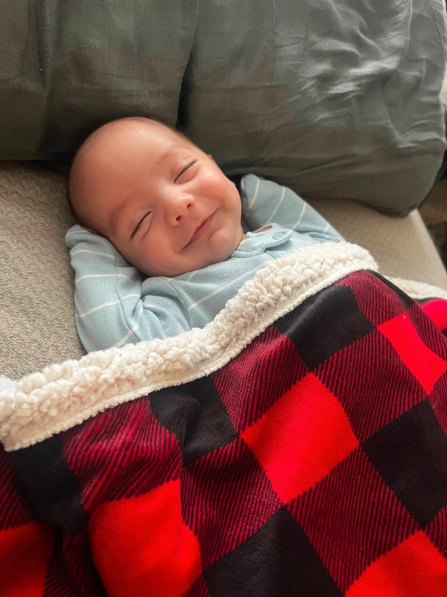 Myles is registered to the contest to win money with this photo: baby, smile, blanket, red, black, checkered, cozy, sleeping, pillow, couch, infant, cute, resting, happy, indoor, person, face, clothing, soft, relaxed