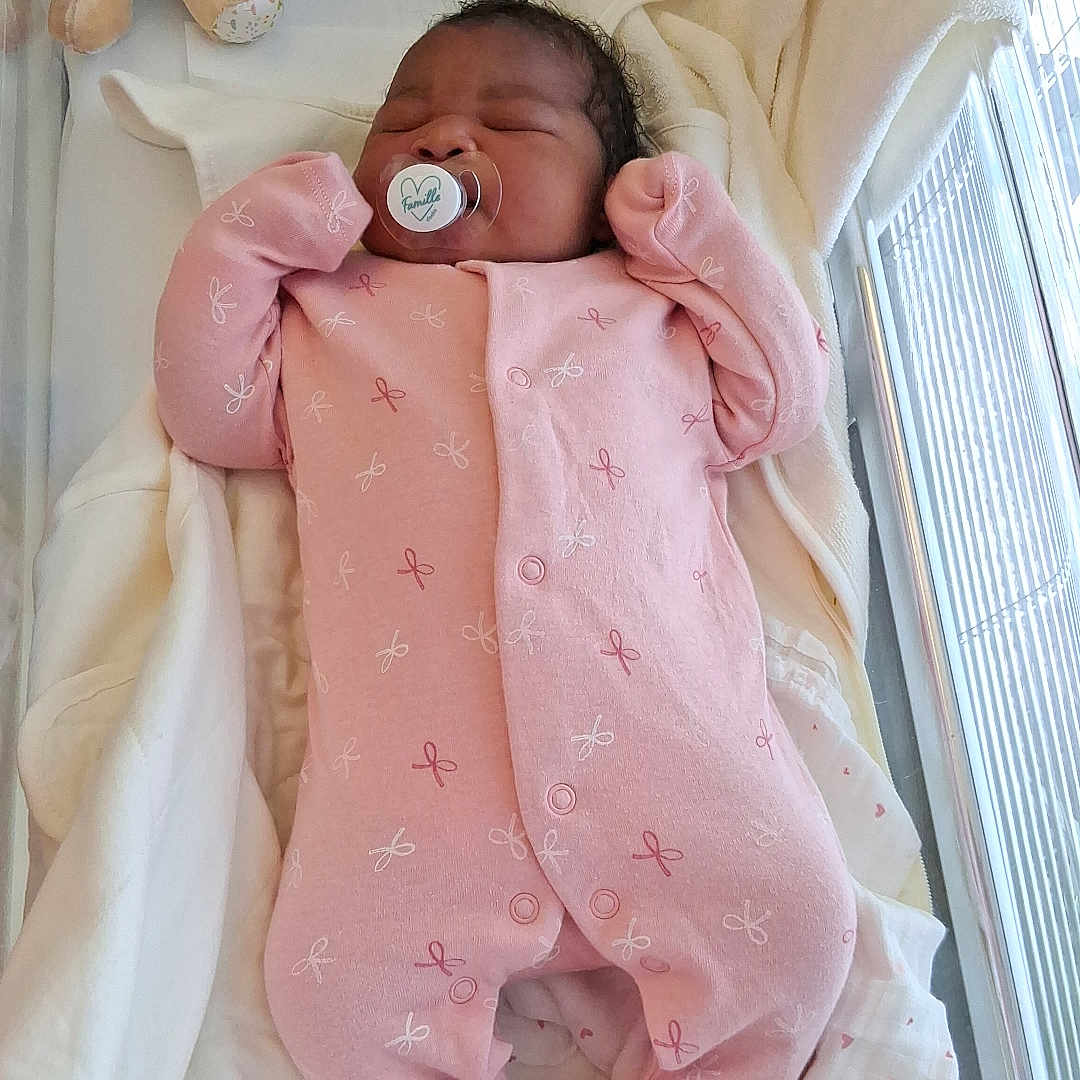 Nelly-Phanuana a rejoint le concours — aidez-le/la à gagner de superbes lots ! baby, bed, blanket, child, cozy, crib, cute, fabric, indoor, infant, newborn, nursery, onesie, pacifier, person, pink_clothing, resting, sleeping, soft_toy, teddy_bear