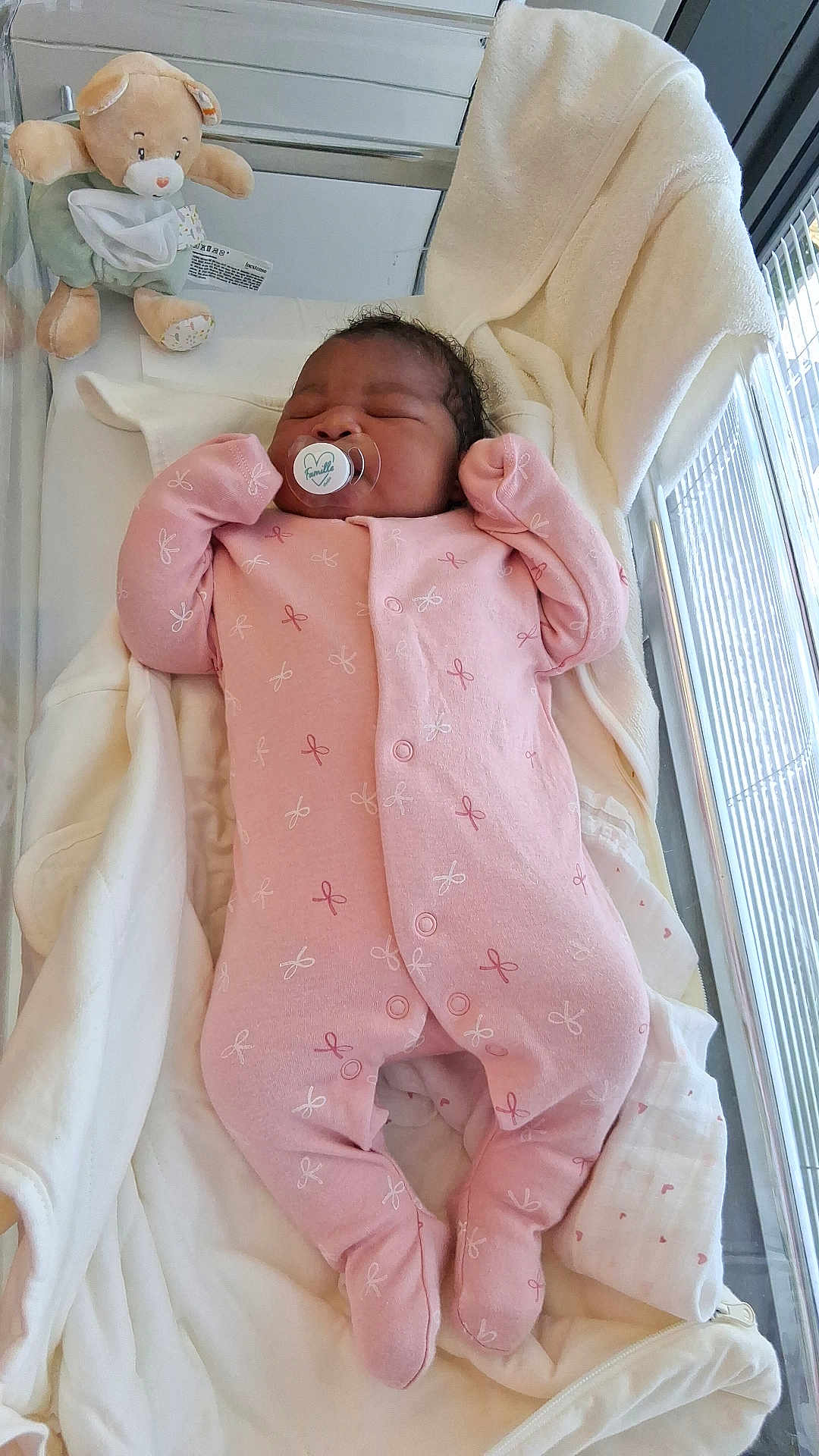 Nelly-Phanuana a rejoint le concours — aidez-le/la à gagner de superbes lots ! baby, newborn, crib, blanket, onesie, pink_clothing, pacifier, sleeping, teddy_bear, soft_toy, nursery, infant, cute, cozy, indoor, child, person, resting, fabric, bed