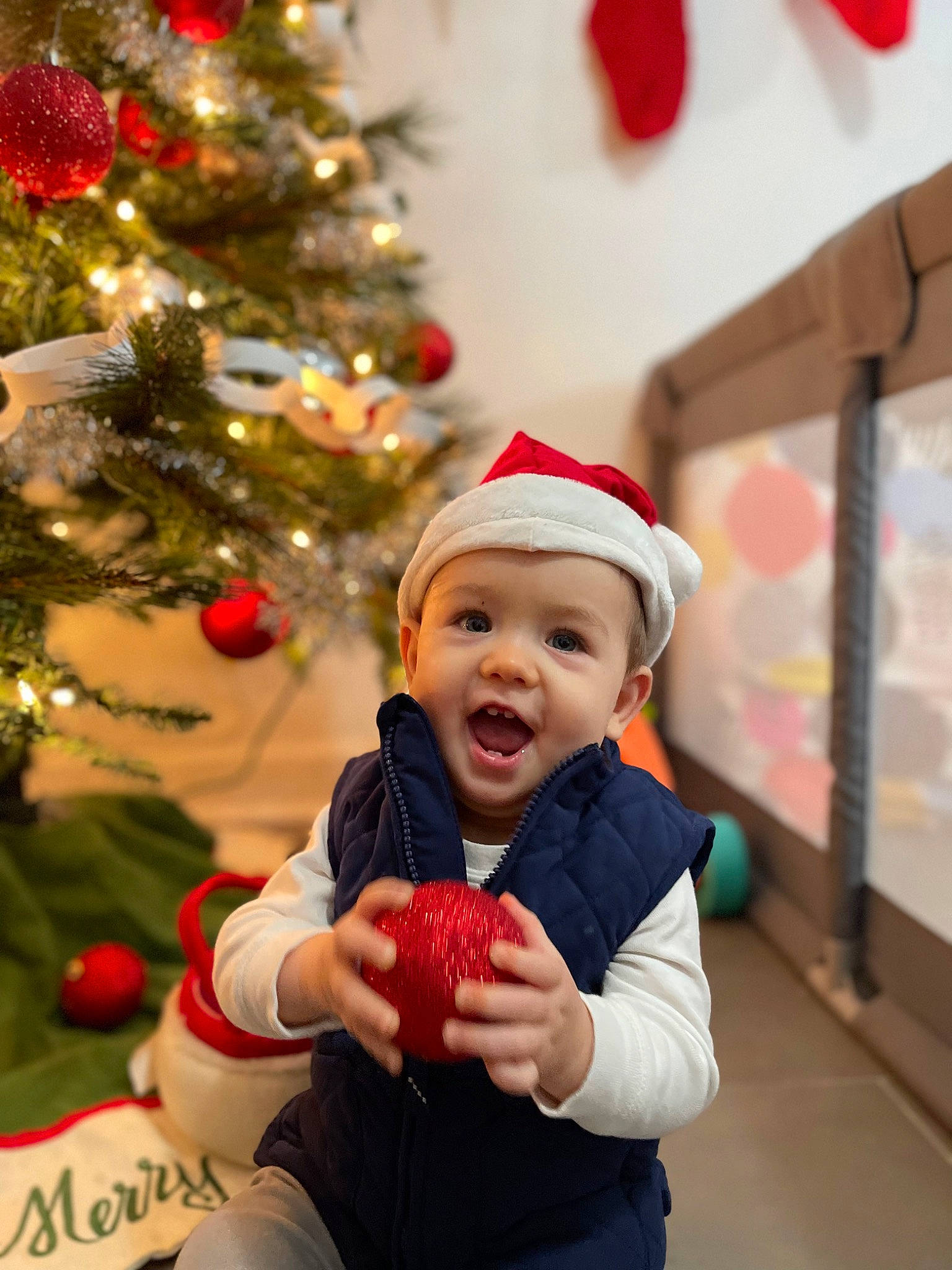 Lucas is registered to the contest to win money with this photo: baby, child, christmas, christmas_decoration, christmas_ornament, christmas_tree, event, fun, happy, headwear, holiday, holiday_ornament, ornament, person, plant, red, room, smile, toddler, tradition