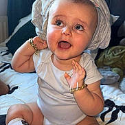 Freddie is registered to the contest to win money with this photo: baby, child, smiling, sitting, bed, towel, onesie, socks, bracelet, happy, indoors, cute, portrait, infant, headwear, expression, skin, person, face, candid