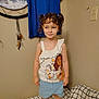 child, girl, pigtails, curly_hair, bed, blanket, blue_shirt, wall, light_switch, smile, standing, clothing, indoor, person, cute, cartoon_top, moana, shorts, furniture, room