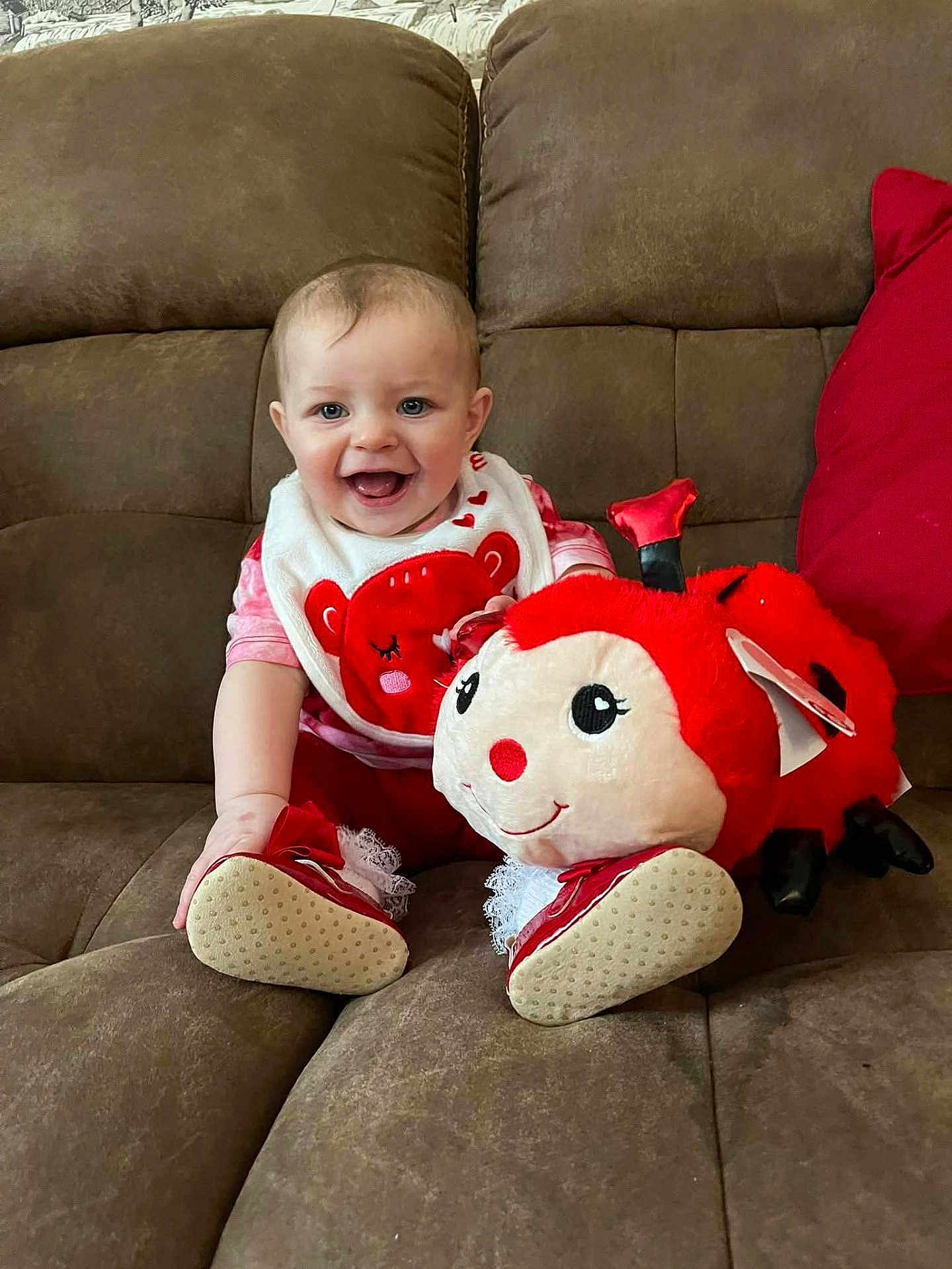 Amelia is registered to the contest to win money with this photo: baby, infant, child, smile, happy, plush_toy, ladybug_toy, red, bib, shoes, couch, sofa, living_room, sitting, portrait, face, cute, clothing, furniture, toy