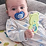 Micky is registered to the contest to win money with this photo: baby, pacifier, toy, cushion, owl_pattern, clothing, infant, lying_down, hand, face, eyes, couch, pillow, blue, green, cute, indoors, child, sleepwear, teether