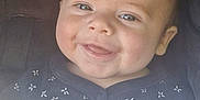 Micky is registered to the contest to win money with this photo: baby, smiling, face, blue_eyes, blanket, clothing, infant, portrait, cute, happy, child, closeup, indoors, seat, car_seat, soft_texture, young, baby_girl_or_boy, skin, expression