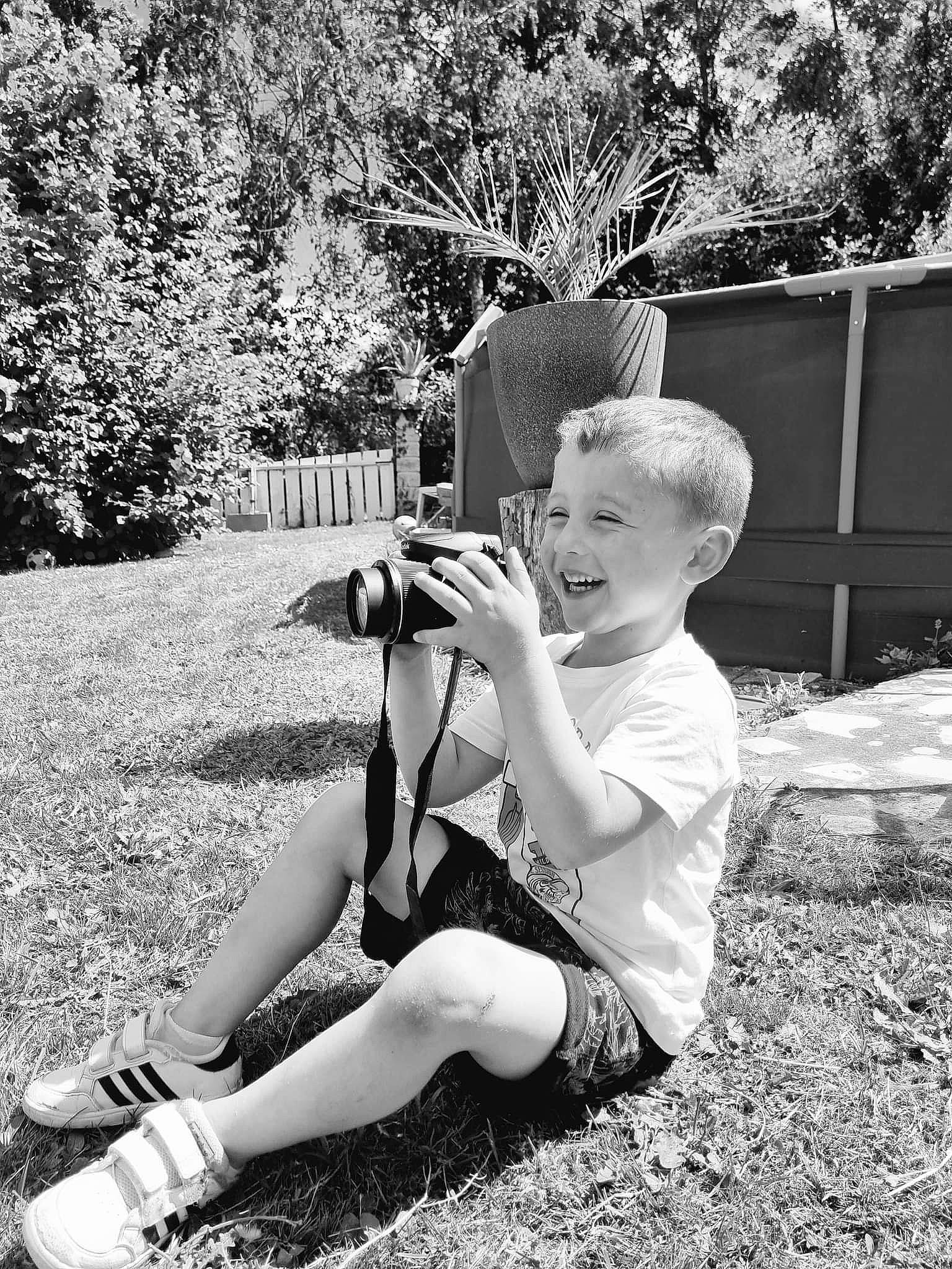 Tiago participe au concours pour gagner de l'argent avec cette photo : black, black_and_white, flash_photography, fun, grass, hairstyle, happy, joy, knee, leg, people, people_in_nature, person, plant, shoe, shorts, sneakers, standing, style, thigh
