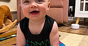 Stetson is registered to the contest to win money with this photo: baby, child, smiling, sitting, rug, indoor, furniture, chair, pillow, rocking_horse, floor, colorful_clothing, happy, person, portrait, home, wood_floor, toy, black_shirt, blue_eyes