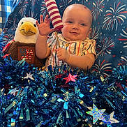 Stetson joined the competition — help win amazing prizes! baby, child, plush_toy, eagle, firework_prop, tinsel, stars, blue_background, striped_shirt, celebration, holiday, smiling, patriotic, decorations, indoor, face, person, festive, cute, red_white_blue