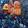 baby, child, plush_toy, eagle, firework_prop, tinsel, stars, blue_background, striped_shirt, celebration, holiday, smiling, patriotic, decorations, indoor, face, person, festive, cute, red_white_blue