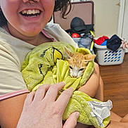 Ponyo is registered to the contest to win money with this photo: person, kitten, cat, orange_and_white, smiling, glasses, portrait, 抱抱, blanket, green_blanket, cuddling, indoor, home, laundry_basket, clothing, hand, arms, pet, cozy, close_up
