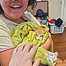 person, kitten, cat, orange_and_white, smiling, glasses, portrait, 抱抱, blanket, green_blanket, cuddling, indoor, home, laundry_basket, clothing, hand, arms, pet, cozy, close_up