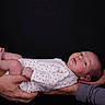 baby, infant, hands, onesie, red_hearts, white_clothing, skin, portrait, newborn, cute, human, child, holding, people, studio, black_background, expression, looking, small, tenderness
