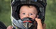 Mattéo participe au concours pour gagner de l'argent avec cette photo : adult_hand, baby, blue_eyes, bokeh, camouflage, child, close_up, cute, expression, face, hand, helmet, holding, infant, motocross_helmet, outdoor, portrait, protective_gear, safety_gear, strap