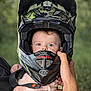 Mattéo participe au concours pour gagner de l'argent avec cette photo : baby, infant, child, face, helmet, motocross_helmet, protective_gear, hand, adult_hand, holding, blue_eyes, portrait, close_up, outdoor, bokeh, camouflage, safety_gear, cute, expression, strap