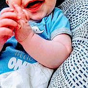 Josiah joined the competition — help win amazing prizes! baby, smiling, blue_shirt, hands, blanket, cushion, patterned, infant, happy, close_up, face, child, cute, resting, indoor, person, soft, cozy, playful, young