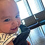 Skylar joined the competition — help win amazing prizes! toddler, child, smile, face, indoor, window, chair, floor, tile_floor, clothing, striped_shirt, person, hand, light, daylight, window_blind, patterned_chair, baby, holding, closeup