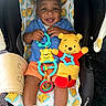 baby, child, smiling, car_seat, toy, plush_toy, winnie_the_pooh, blue_shirt, orange_shorts, white_socks, baby_toys, infant, cute, happy, indoor, person, playful, seat, fabric, accessory