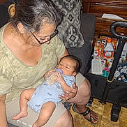 Lucas is registered to the contest to win money with this photo: baby, bottle, feeding, woman, glasses, hair, chair, cushion, clothing, footwear, floor, furniture, indoor, person, skin, hand, baby_supplies, telephone, printer, cart
