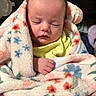 baby, sleeping, blanket, floral_pattern, soft_texture, cozy, infant, wrapped, hand, yellow_clothing, indoor, peaceful, cute, newborn, portrait, closeup, warm, comfort, resting, child