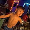 child, boy, shirtless, shorts, christmas_tree, ornaments, lights, holiday, indoor, decorations, curious, face, smiling, home, cozy, colorful_lights, evening, celebration, young, festive