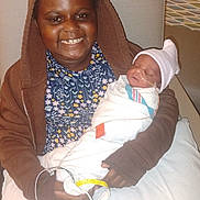 Josiah is registered to the contest to win money with this photo: child, newborn, baby, hospital, blanket, hoodie, smile, medical, bed, person, infant, sleeping, patient, wires, hat, young, holding, family, portrait, indoors