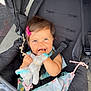 baby, child, stroller, toy, stuffed_animal, pink_bow, smiling, happy, cute, infant, seatbelt, outdoor, dress, person, face, hands, playful, cheerful, bright, daylight