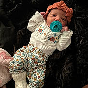 Alayah is registered to the contest to win money with this photo: baby, pacifier, headband, knitted_booties, floral_pants, white_sweater, blanket, infant, cute, cozy, sleepy, portrait, child, soft_texture, resting, indoors, small_hands, patterned_clothing, warm_clothing, relaxed
