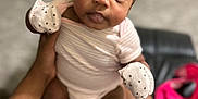 Alayah is registered to the contest to win money with this photo: baby, infant, mittens, onesie, tattoo, hand, legs, person, indoor, carpet, blurred_background, cute, child, skin, face, eyes, sitting, holding, human, soft_lighting