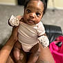 baby, infant, mittens, onesie, tattoo, hand, legs, person, indoor, carpet, blurred_background, cute, child, skin, face, eyes, sitting, holding, human, soft_lighting