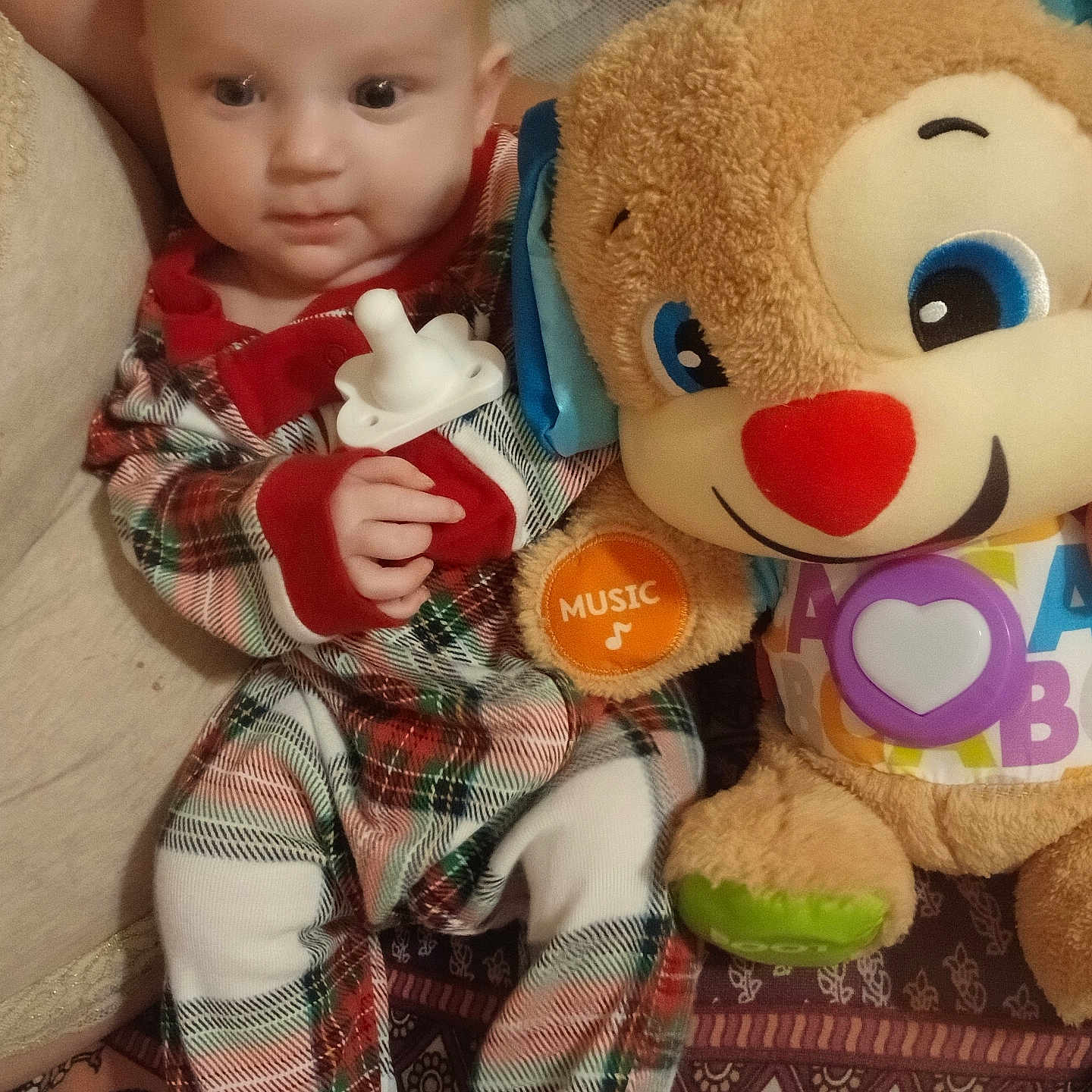 Octavia is registered to the contest to win money with this photo: baby, child, comfort, cute, fabric, face, footwear, hand, indoor, infant, pacifier, pajamas, pattern, plaid, plush_toy, red, seated, soft_toy, toy, white
