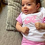 baby, infant, smiling, pink_clothing, white_shirt, nike_logo, pillow, soft_texture, lying_down, cute, cheeky, indoors, skin, face, hands, shorts, comfortable, child, young, portrait