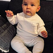 Elio participe au concours pour gagner de l'argent avec cette photo : baby, child, infant, sitting, white_clothing, knitwear, couch, pillow, indoor, cute, face, expression, hands, footwear, soft_lighting, portrait, young_child, cozy, curious, casual