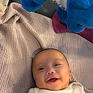 Danielle Anaia is registered to the contest to win money with this photo: baby, infant, child, smiling, happy, portrait, lying_down, blanket, quilt, stuffed_animal, plush_toy, blue_toy, onesie, home, indoor, cozy, bed, bedding, face, photography