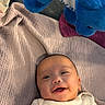 baby, infant, child, smiling, happy, portrait, lying_down, blanket, quilt, stuffed_animal, plush_toy, blue_toy, onesie, home, indoor, cozy, bed, bedding, face, photography