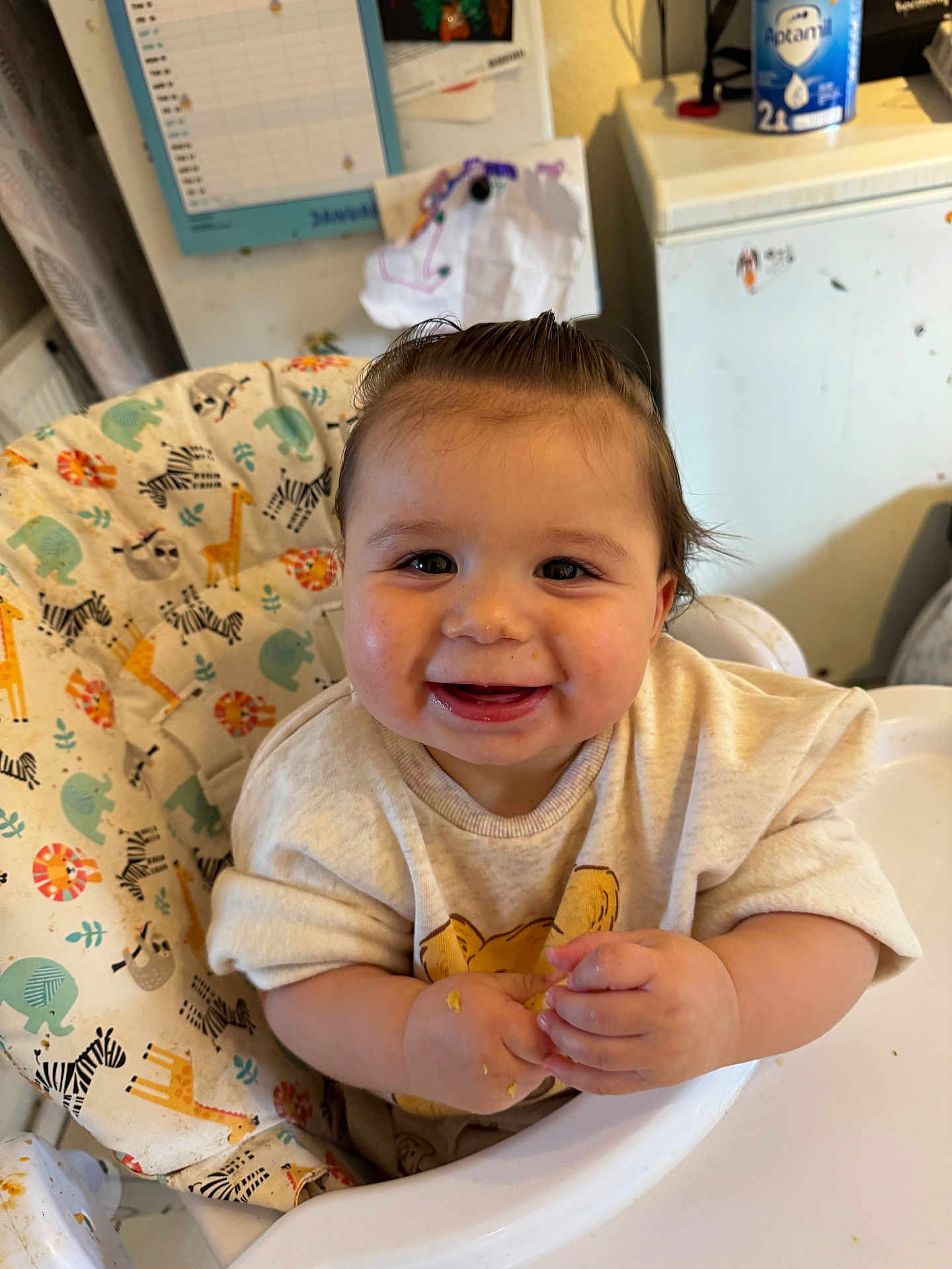 Ayaz joined the competition — help win amazing prizes! baby, infant, smile, high_chair, messy_hands, food, adorable, portrait, indoor, kitchen, refrigerator, animal_print, giraffe, zebra, cheeks, feeding, clothing, milk_tin, calendar, happy