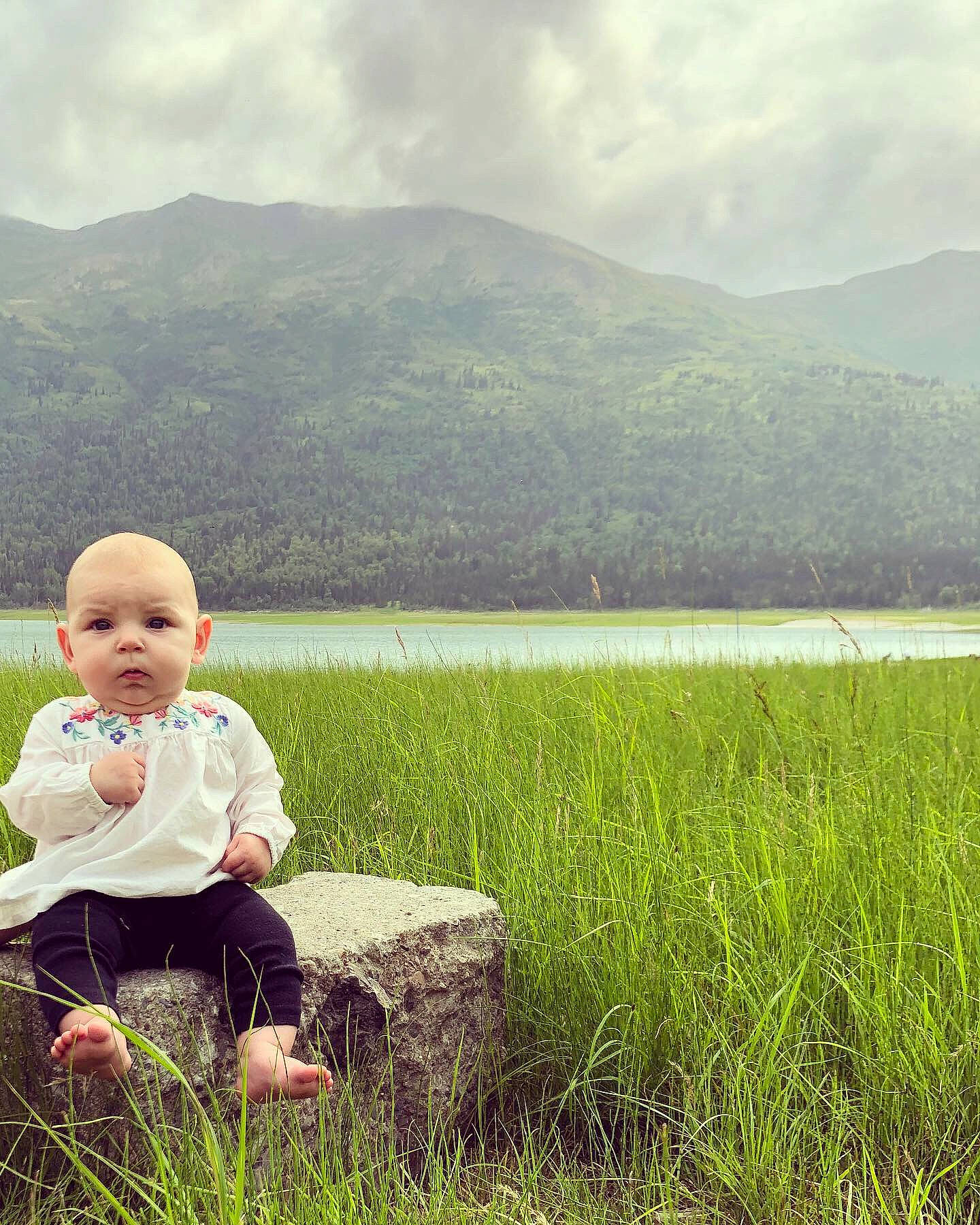 Aryanna joined the competition — help win amazing prizes! child, cloud, grass, grass_family, grassland, green, happy, meadow, mountain, natural_landscape, paddy_field, people_in_nature, person, photography, rural_area, sitting, sky, smile, spring, toddler