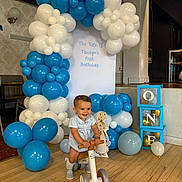 Thiago joined the competition — help win amazing prizes! balance_bike, balloons, birthday, blocks, blue, celebration, child, cute, decor, event, floor, happy, indoor, party, person, riding, smile, toddler, toy, white