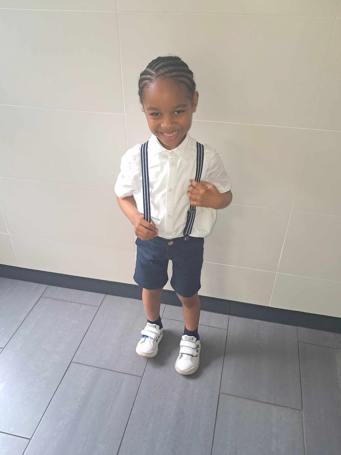 Jemmy a rejoint le concours — aidez-le/la à gagner de superbes lots ! boy, braided_hair, casual_clothing, child, cute, fashion, floor_tiles, footwear, happy, indoors, person, portrait, shorts, smile, sneakers, standing, suspenders, wall, white_shirt, young