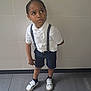 boy, casual, casual_clothing, child, curious, floor, footwear, indoor, looking_up, navy_shorts, person, portrait, shorts, socks, standing, suspenders, tiles, wall, white_shirt, white_shoes