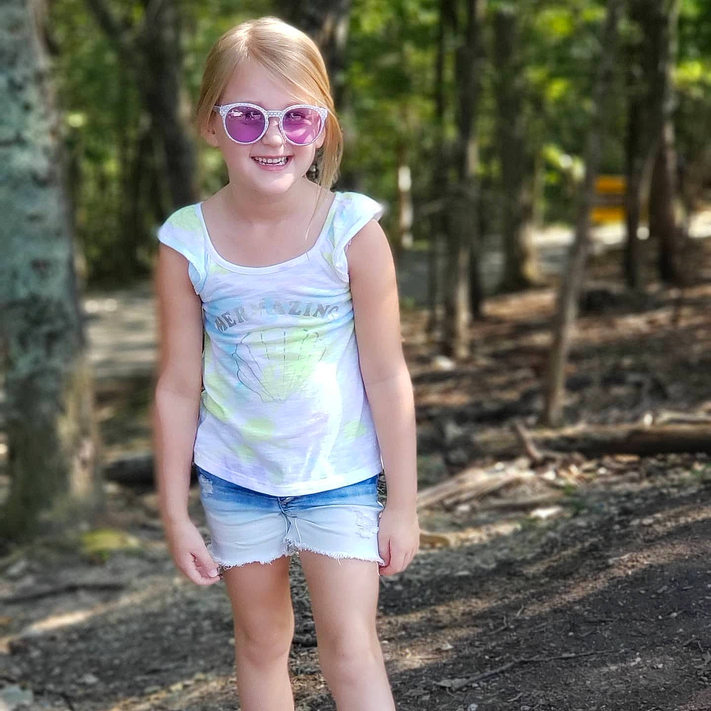 Jacqueline is registered to the contest to win money with this photo: clothing, eye, face, facial_expression, goggles, hair, hairstyle, happy, head, joy, leaf, people_in_nature, person, plant, shorts, shoulder, standing, street_fashion, sunglasses, sunlight