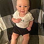Alden is registered to the contest to win money with this photo: baby, child, smiling, sitting, white_shirt, black_shorts, checkered_blanket, indoor, cute, happy, face, legs, feet, socks, shoes, person, infant, portrait, looking_at_camera, hand