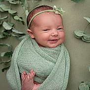 Layla joined the competition — help win amazing prizes! baby, newborn, smiling, wrapped, blanket, headband, green, soft_texture, feet, face, portrait, cute, infant, peaceful, plant, leaves, closeup, indoors, child, adorable