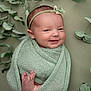 baby, newborn, smiling, wrapped, blanket, headband, green, soft_texture, feet, face, portrait, cute, infant, peaceful, plant, leaves, closeup, indoors, child, adorable