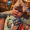 baby, child, headband, bow, onesie, indoor, warm_lighting, person, face, expression, holding, patterned_clothing, lamp, wooden_furniture, cozy, curious, infant, portrait, candid, closeup