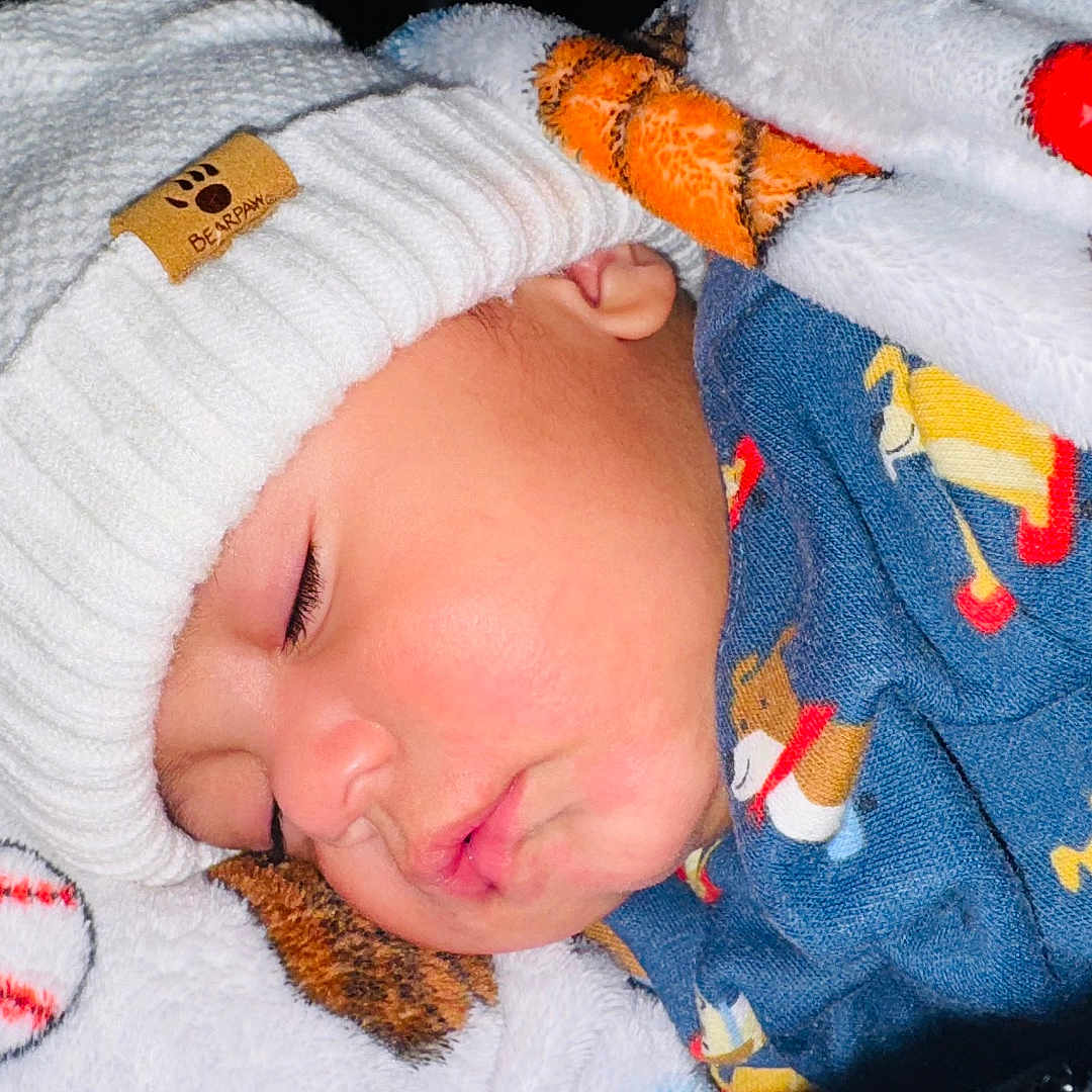 Yasser Izam is registered to the contest to win money with this photo: baby, blanket, child, closeup, clothing, comfort, cozy, cute, dog_pattern, face, hat, indoors, infant, knit_hat, peaceful, portrait, rest, sleeping, soft, warm