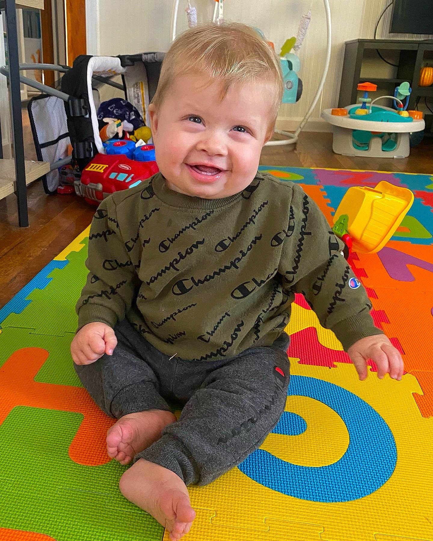 Jaxon is registered to the contest to win money with this photo: baby, baby_toddler_clothing, carpet, chair, child, floor, flooring, fun, home_appliance, kitchen_appliance, pattern, person, play, playmat, product, room, sitting, smile, television, toddler
