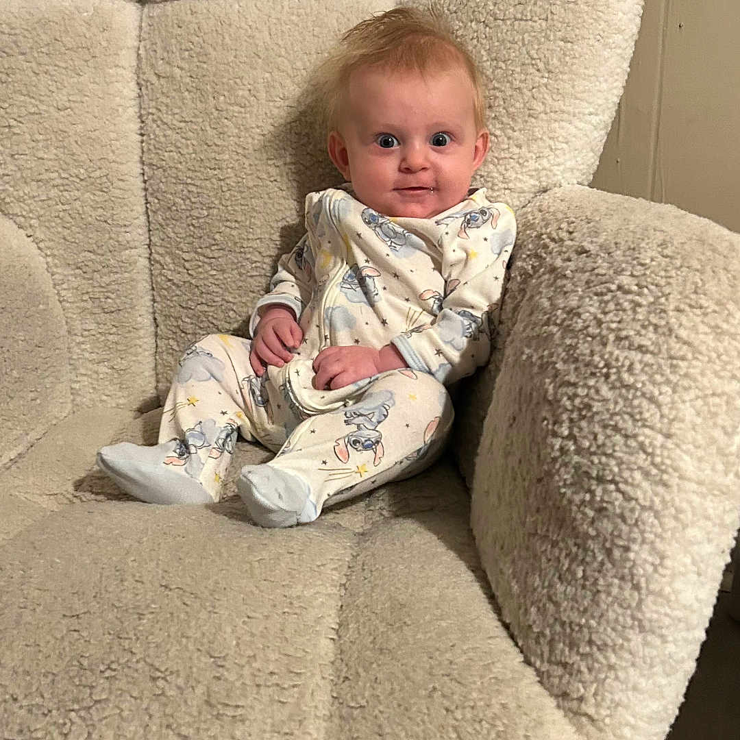 Emerson is registered to the contest to win money with this photo: armchair, baby, child, cozy, curious, cute, expression, face, furniture, home, indoor, infant, light, looking, pajamas, person, plush, seated, smile, soft
