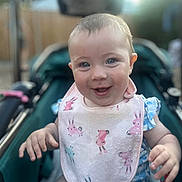 Skylah is registered to the contest to win money with this photo: baby, smiling, bib, bunny_pattern, blue_outfit, stroller, happy, child, infant, face, hands, outdoor, daylight, cute, portrait, clothing, person, skin, head, eyes