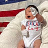 american_flag, baby, blanket, blue_shoes, child, cute, fabric, flag, happy, indoor, infant, lying_down, mittens, newborn, onesie, portrait, smiling, stars, stripes, white_clothing